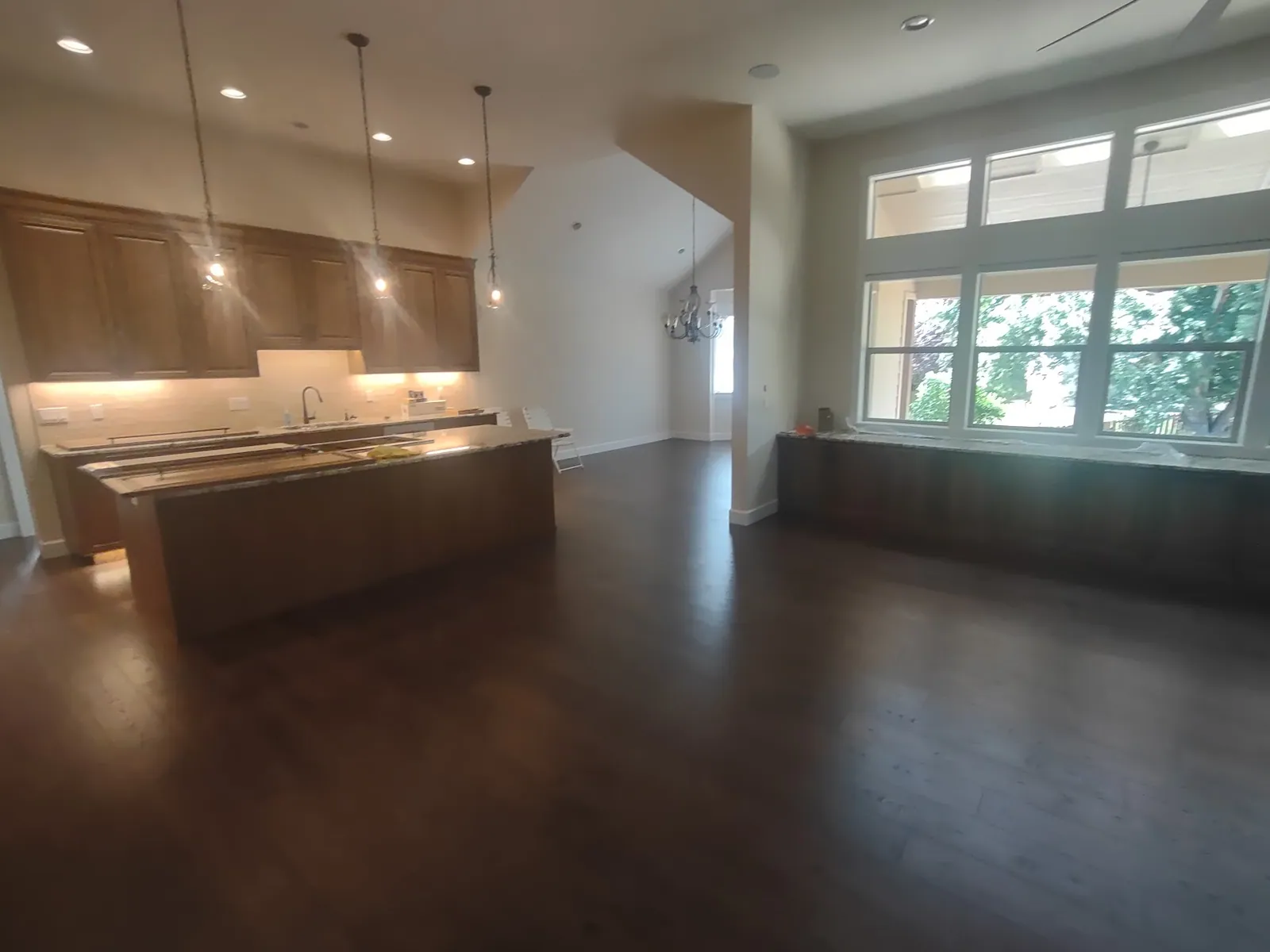 Open great room and kitchen with pendant lights and dark wood floors