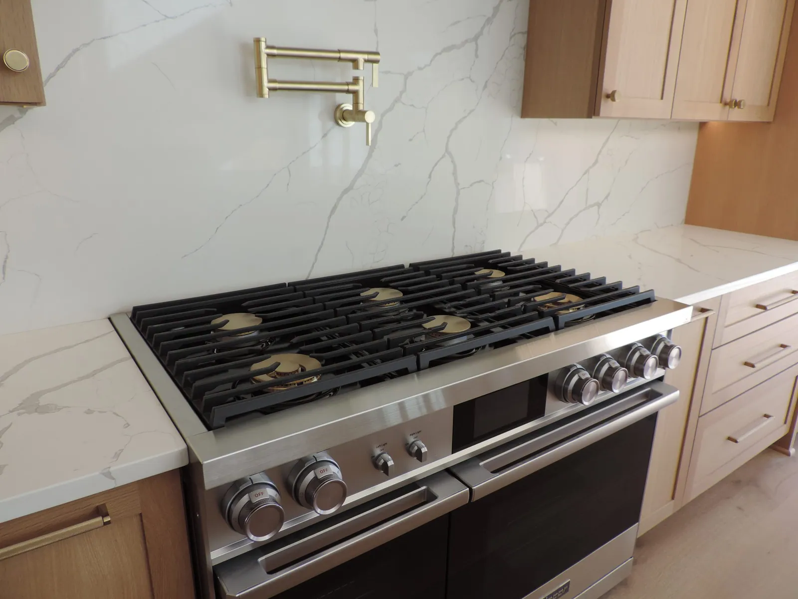 Professional range with a brass pot filler and marble-look backsplash
