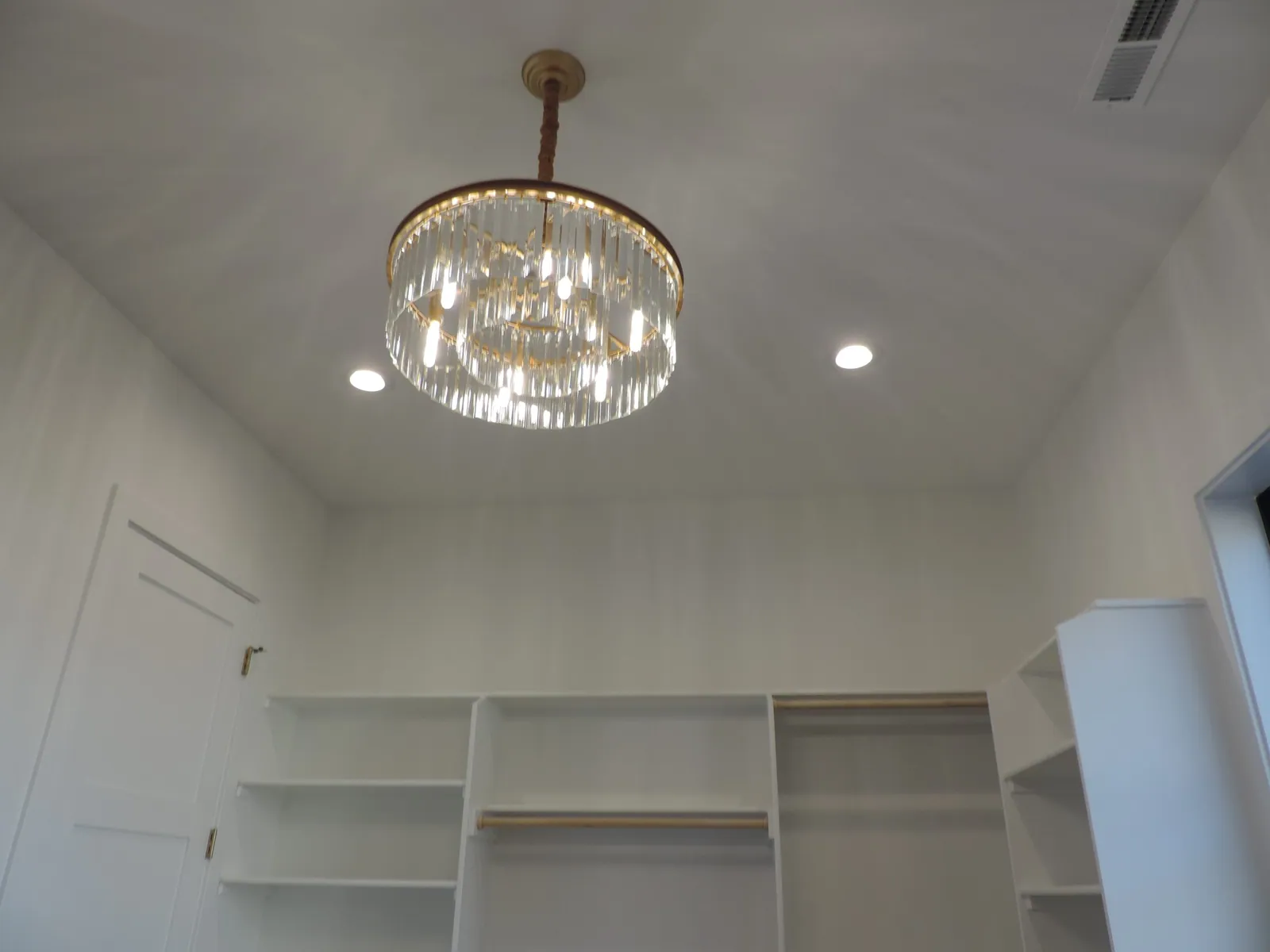 Walk-in closet with white shelving and a crystal chandelier