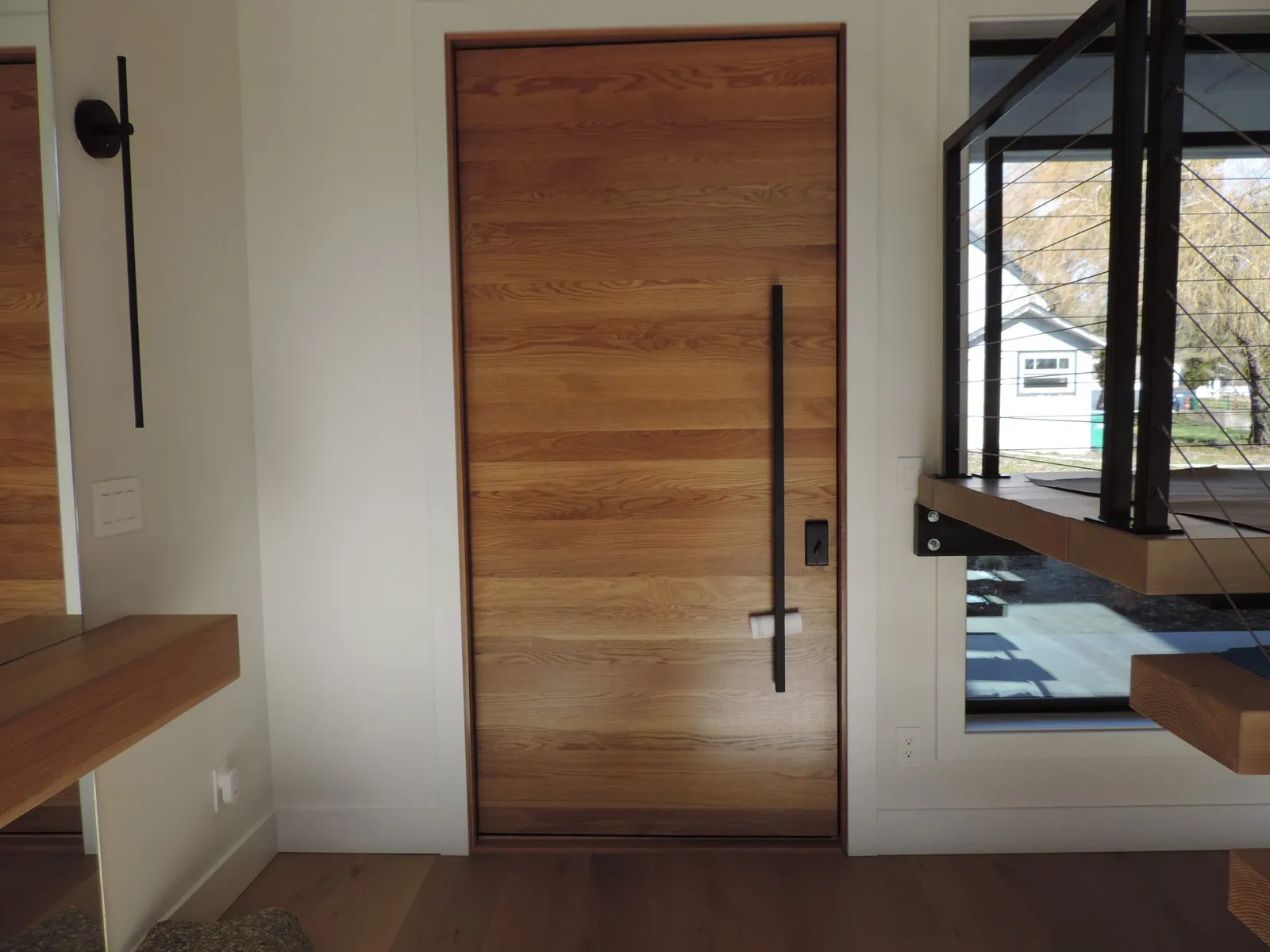 White oak entry door with black hardware and a floating bench