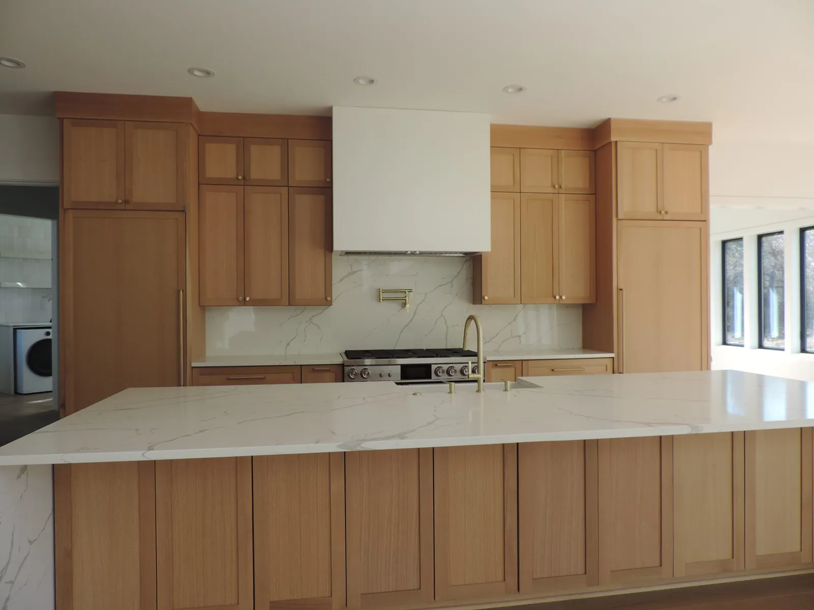 White oak kitchen with a long quartz island and brass fixtures in the same farmhouse