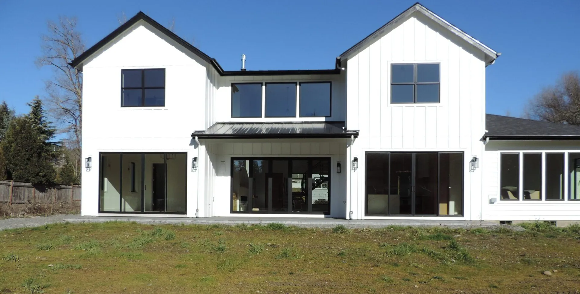 White board-and-batten custom farmhouse with black-framed windows under a clear blue sky